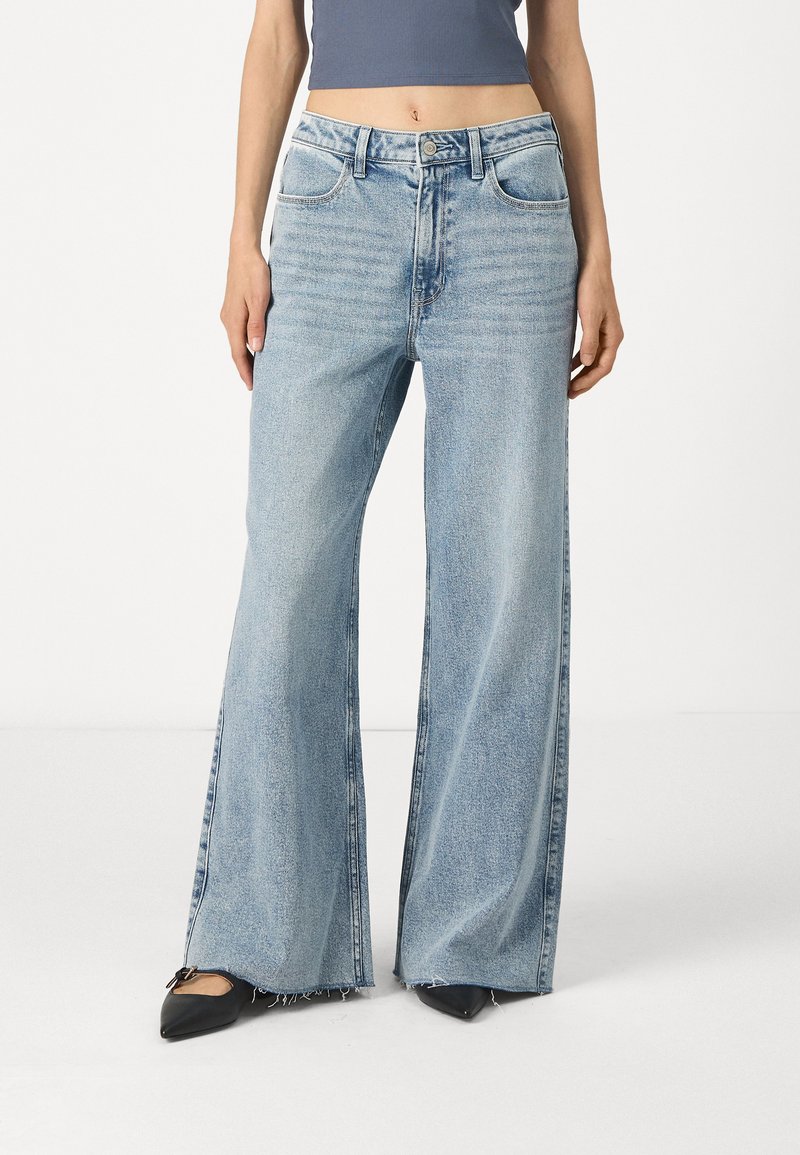 Ανοιχτό μπλε τζιν παντελόνι σε φαρδύ στιλ, φτιαγμένο από τζιν ύφασμα, με ψηλή μέση, μπροστινές τσέπες και ξεφτισμένο στρίφωμα. Φοριέται με μαύρες μυτερές γόβες.