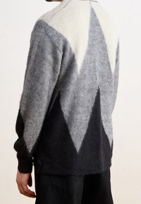 Ullkardigan med diamantmönster i grått, krämfärgat och svart. Har långa ärmar, rundad halsringning och en avslappnad passform.