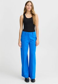 Zilas platās bikses ar priekšējiem krokām un gludu tekstūru, apvienotas ar melnu pieguļošu topu bez piedurknēm. Vienkāršs dizains, bez rakstiem vai rotājumiem.