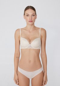 Beige Spitzen-BH mit gepolsterten Cups und verstellbaren Trägern, mit einer gewellten Kante am oberen Rand. Passende bequeme Unterwäsche in Beige.