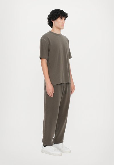 Oliven grøn kortærmet t-shirt og matchende joggers, lavet af blødt stof, løs pasform, med sidelommer, parret med hvide sneakers.