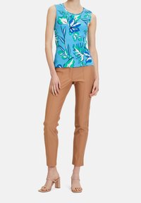 Top sin mangas floral en azul, verde y blanco con escote redondeado, combinado con pantalones ajustados color beige. Sandalias de tacón bloque beige con tiras.