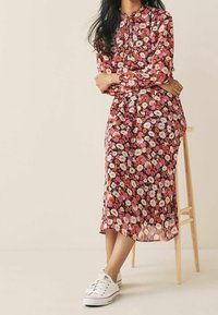 Robe midi fleurie en tissu transparent, présentant un mélange de fleurs roses, rouges et blanches. Associée à des baskets blanches, mettant en avant un style décontracté.