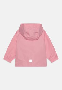 Giacca impermeabile rosa con cappuccio; maniche lunghe, polsini elasticizzati e un'etichetta quadrata bianca sul retro. Tessuto liscio.
