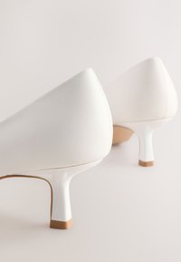 Hvide læderstiletter med spidst tådesign. Har en blank hvid hæl og en lysebrun gummisål.