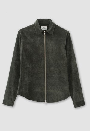 Veste chemise en velours côtelé vert foncé avec un col, des manches longues et une fermeture éclair à l'avant. Texture lisse avec de subtiles variations de couleur.