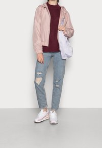 Veste à capuche rose clair, pull en tricot bordeaux, jeans déchirés bleu clair et baskets blanc-rose. Fond gris. Sac à épaule simple.