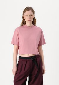 Kuttet rosa t-skjorte laget av myk stoff, med kort erm og rund hals. Kombinert med mørk burgunder høyere midjebukser.