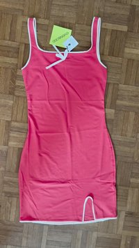 Rosa Kleid mit taillierter Form, weißen Akzenten und einer Frontbindeschleife. Aus glattem Stoff mit einem seitlichen Schlitz am Saum. Tags angebracht.