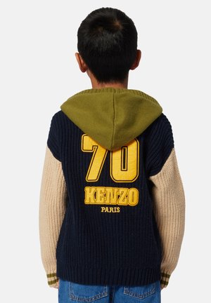 Gebreide trui met een groene capuchon, een marineblauwe romp en beige mouwen. Heeft een groot gele "70" en "KENZO PARIS" op de achterkant.