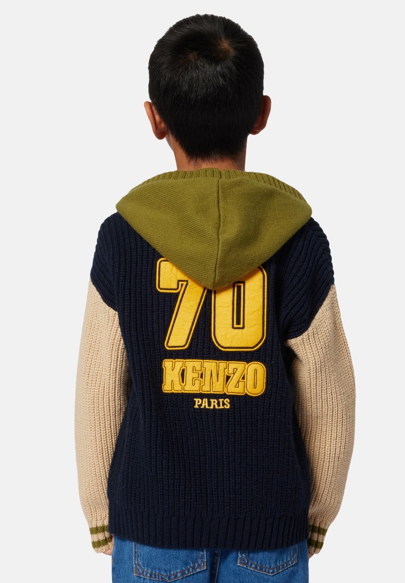 Pull en laine avec une capuche verte, un corps marine et des manches beiges. Il arbore un grand "70" jaune et "KENZO PARIS" au dos.