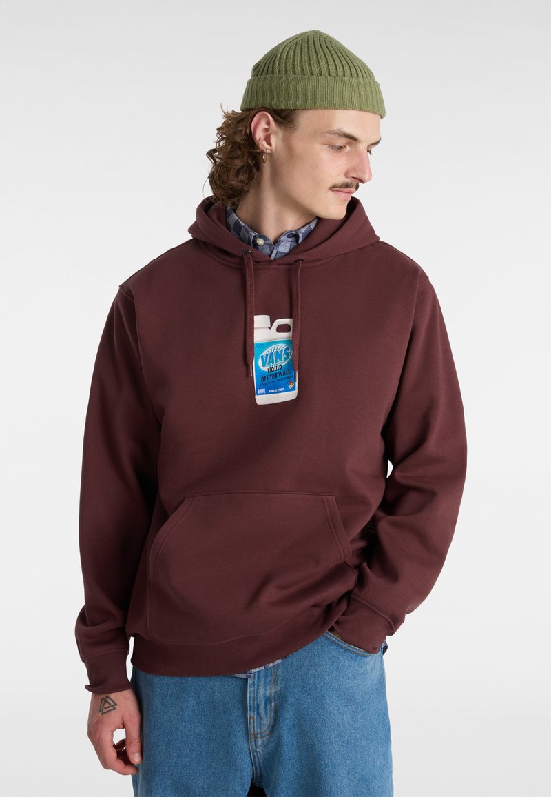 Vinchansad mörkröd hoodie med framlapp och en vit och blå grafisk etikett, kombinerad med ljusblå denimbyxor och en grön stickad mössa.