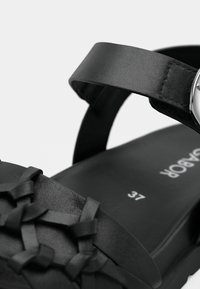 Μαύρο δερμάτινο σανδάλι με υφαντό σχέδιο ιμάντα, ρυθμιζόμενο λουράκι αστραγάλου και επενδεδυμένη σόλα με ορατή ετικέτα μεγέθους.