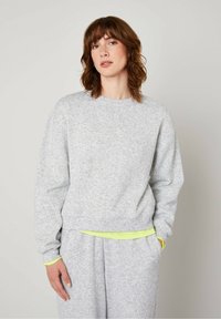 Light grey sweatshirt made of fleece, featuring a crew neck, ribbed cuffs, and a layered neon green trim at the hem.