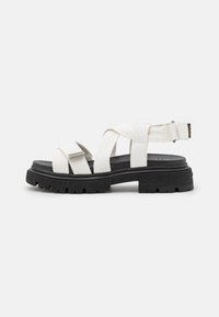 Witte platform sandalen met kruislingse stoffen banden, een gestructureerd oppervlak en een dikke zwarte rubberen zool met een profiel.