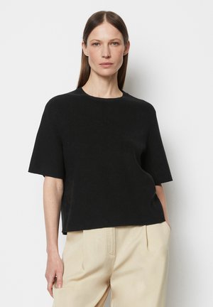 Schwarzes kurzärmliges, geripptes Strickshirt mit Rundhalsausschnitt, lockerer Passform und glatter Textur, kombiniert mit beigen, hoch taillierten Hosen.