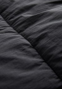 Fekete steppelt szövet, amely sima textúrát mutat finom fényességgel és lágy redőkkel, kiemelve az anyag könnyű és otthonos megjelenését.