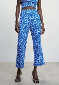 Modré kalhoty s květinovým vzorem vyrobené z lehkého materiálu, s širokými nohavicemi a vysokým pasem. V kombinaci s odpovídajícím topem a sandály.