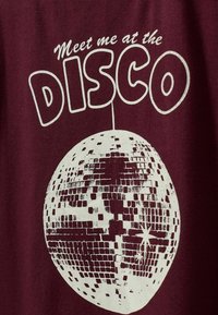 Burgunder T-Shirt mit einem weißen Grafikdesign eines Discokugels und dem Text "Treff mich am DISCO" in einer auffälligen, verspielten Schriftart.
