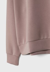 Gros plan sur la manche d'un sweat-shirt mauve et l'ourlet côtelé montrant la texture douce du tissu et des coutures nettes.