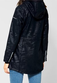 Veste à capuche camouflage noire en tissu texturé, avec des manches longues et des accents réfléchissants aux poignets.