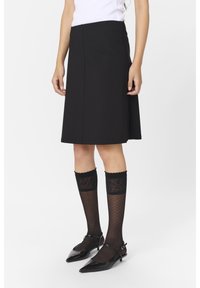 Gonna nera a trapezio realizzata in tessuto liscio, abbinata a calze nere a righe al ginocchio e scarpe nere a punta con cinturino alla caviglia.