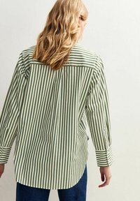Green and white striped button-up shirt with long sleeves and a curved hem. Features a back yoke and roll-tab sleeves for adjustable fit.