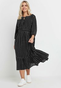 Svart klänning med vita fyrkantiga mönster, elastisk midja, långärmad och utsvängd kjol. Kombinerad med vita sneakers. Flödande tygstruktur.