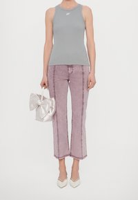 Szary bezrękawnik z logo, jasnofioletowe dżinsy z wysokim stanem, biała satynowa torebka z dużą kokardą oraz białe buty na obcasie z ostrym noskiem.