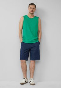 Grünes Baumwoll-Ärmelloses Shirt, Jeansshorts und weiße Sneaker mit braunen Akzenten. Lässiges Outfit geeignet für warmes Wetter.