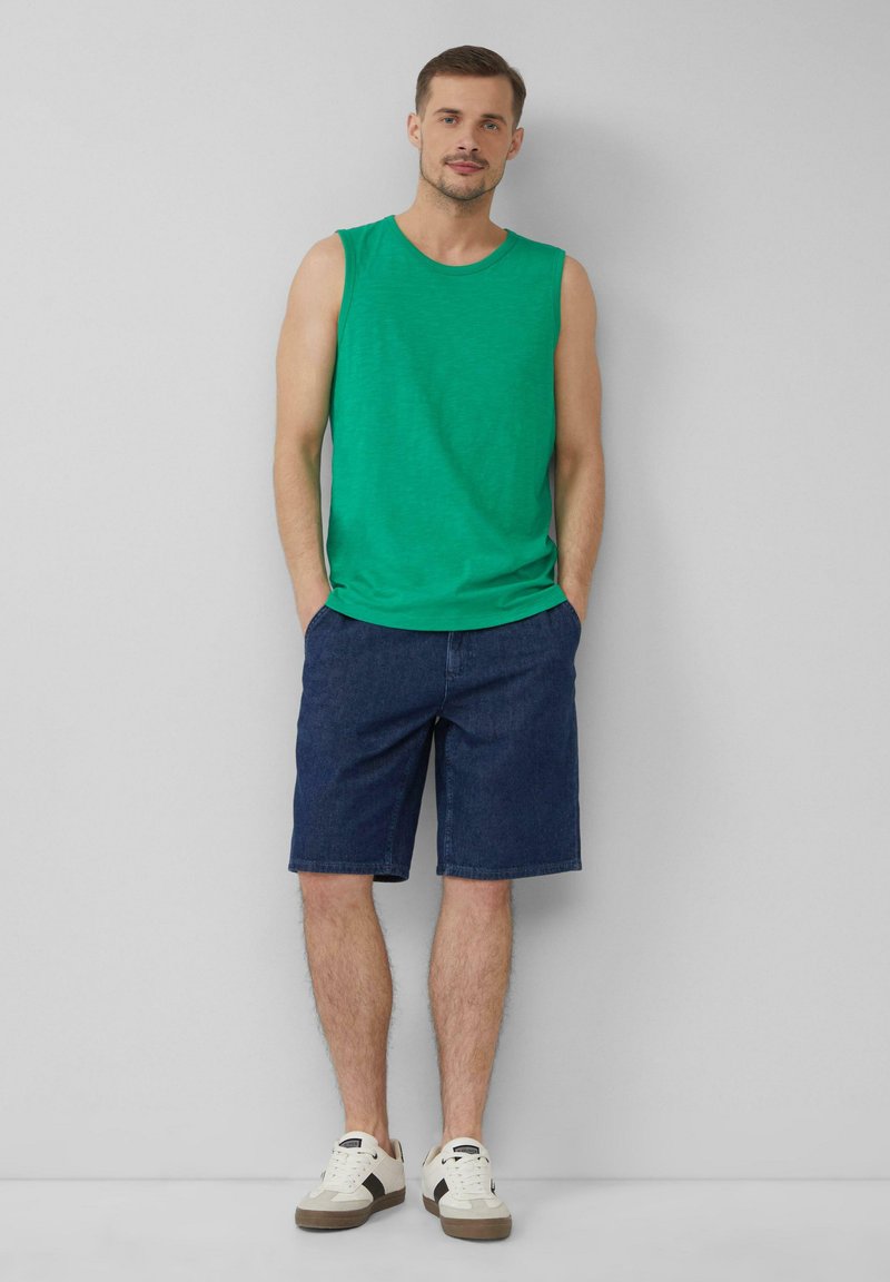 Grünes Baumwoll-Ärmelloses Shirt, Jeansshorts und weiße Sneaker mit braunen Akzenten. Lässiges Outfit geeignet für warmes Wetter.