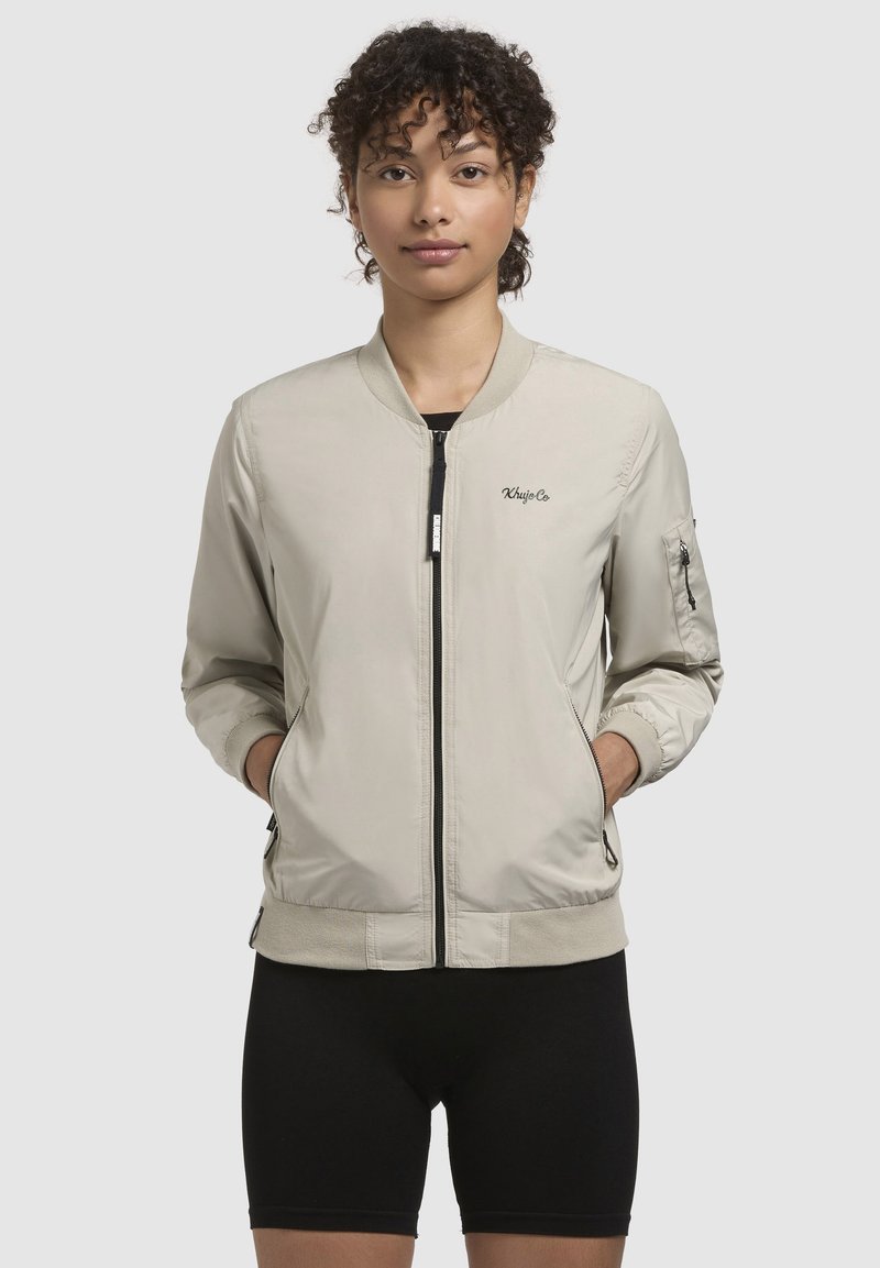 Heledbeez bomber-jakk, millel on ees lukuga tõmblukud, äärised ja allääre soonilised, tikitud logo rinnal ning küljetaskud. Sile kangas.