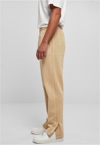 Beige bomulds joggers med en afslappet pasform, elastisk talje, sidelommer og pæne syninger, parret med hvide sneakers.