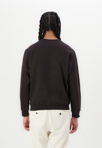 Mørkebrun sweatshirt med lange ærmer og ribbede manchetter, vist fra ryggen. Blød tekstur, enkelt design, tætsiddende talje.