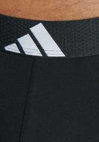 Svart atletisk midjeband med texturerad väv och tre vita diagonala ränder. Huvuddelen är slät och figurnära.