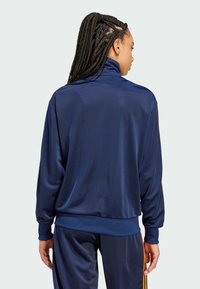 Marineblaues Satin-Trainingsjackett mit hohem Kragen, langen Ärmeln und elastischen Bündchen. Glatte Textur, minimale Details und lässige Passform.