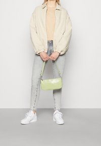 Bolso verde con estampado de cocodrilo, de diseño delgado y correa corta. Combinado con una blusa beige, chaqueta oversized, vaqueros grises y zapatillas blancas.