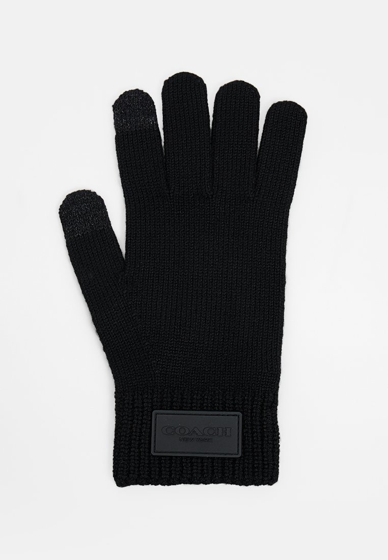 Guantes de punto negros con un puño acanalado, que presentan un material texturizado y un parche rectangular negro etiquetado "COACH" en la muñeca.