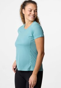 Top atletico azzurro chiaro con maniche corte, texture liscia, scollatura rotonda e sottili righe verticali. Indossato con leggings neri.
