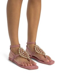 Sandali piatti in suede rosa con decorazioni di cristalli sulla fascia superiore e un design minimalista a infradito.