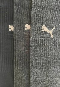 Drei Paar gerippte Socken in Schwarz, Dunkelgrau und Hellgrau, jeweils mit einem weißen Puma-Logo nahe der Oberseite.
