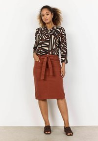 Blusa a maniche lunghe con fantasia astratta in nero, beige e ruggine; gonna aderente ruggine con cintura a fiocco; mule aperti beige.