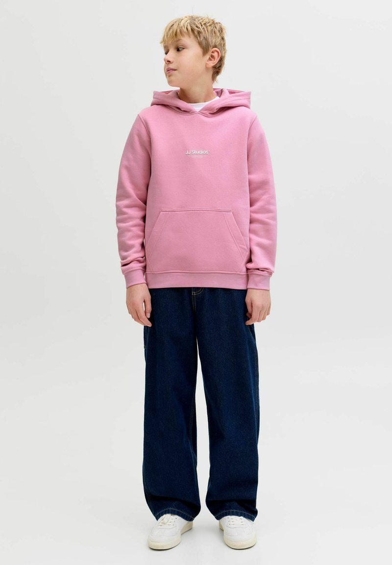 Lyserød sweatshirt med hætte og kængurulomme, med hvidt logo. Kombineret med løse blå jeans og hvide sneakers.
