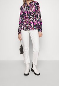 Blusa floreale a maniche lunghe nei toni del nero, rosa e viola. Abbinata a pantaloni bianchi a gamba dritta e stivaletti bianchi con suola nera.
