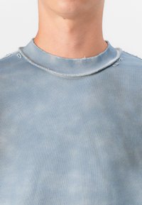 Sweatshirt azul claro com decote redondo, bordas desfiadas e textura desbotada. O material parece suave, com variações sutis na cor.