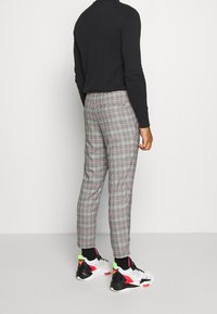Szare spodnie w kratę o slim fit, z czarnymi akcentami i teksturowanym materiałem. Połączone z kolorowymi, sportowymi sneakersami.