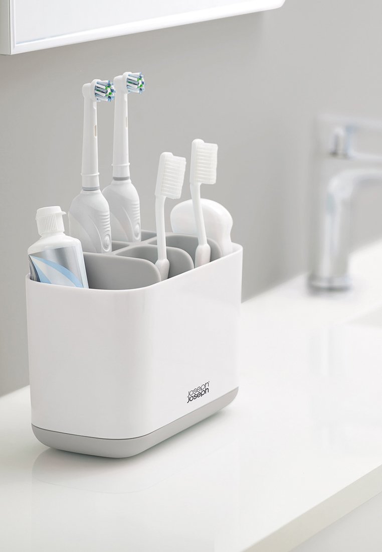 Weißer Zahnbürstenhalter mit grauem Fuß, ausgestattet mit Fächern für zwei elektrische Zahnbürsten, zwei manuelle Zahnbürsten und eine Zahnpastatube.