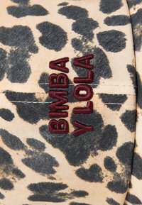 Leparda raksta audums bežā un melnā krāsā ar izšūtu "BIMBA Y LOLA" tekstu bordo krāsā. Tekstūrēta virsma ar redzamām šuvēm.