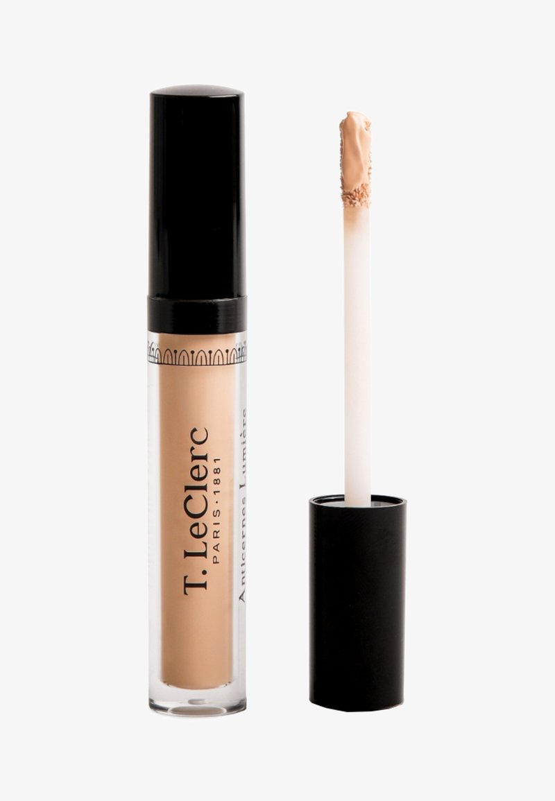 Flüssiger Concealer in einem transparenten Röhrchen mit schwarzem Deckel. Der Applikator ist ein weißer Fußapplikator, mit einem hellbeigen Produkt an der Spitze.