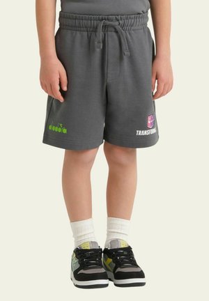 Bambino che indossa pantaloncini grigi scuro con vita elastica e loghi verdi e rosa, calzini bianchi e scarpe da ginnastica nere e grigie con dettagli colorati.